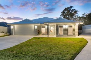 Modern single-story home facade with lit entry and attached garage at dusk.