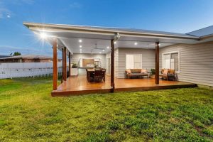 Backyard patio with a wooden deck under a covered porch, featuring an outdoor dining table, seating, and a grill area.