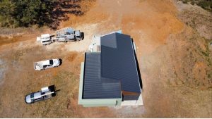Aerial view of a modern house under construction on a dirt lot with several trucks nearby.