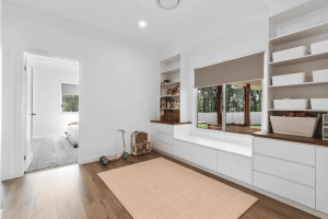 Bright playroom with white built-in cabinets, window seat, and shelves holding baskets; toys on a peach rug.