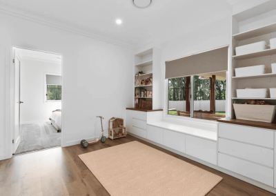 Bright playroom with white built-in cabinets, window seat, and shelves holding baskets; toys on a peach rug.